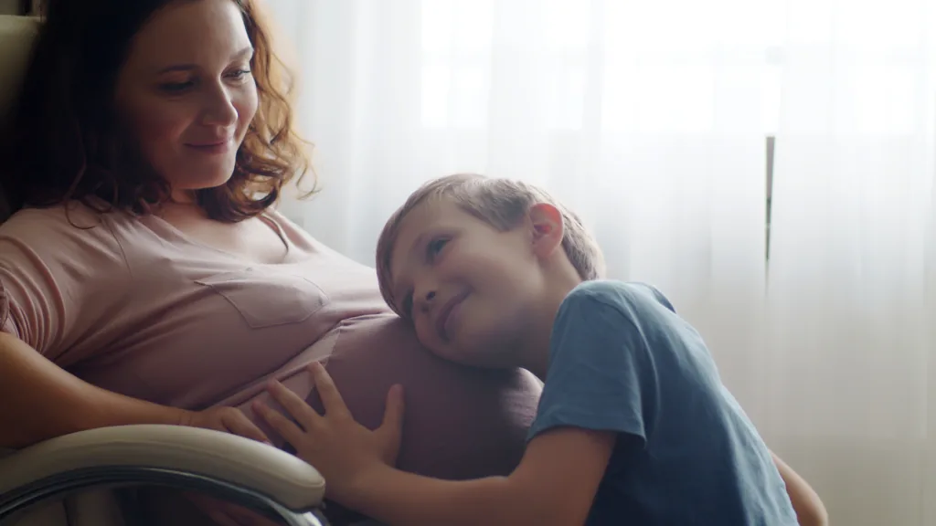 A young boy resting his head against his pregnant mother&rsquo;s belly