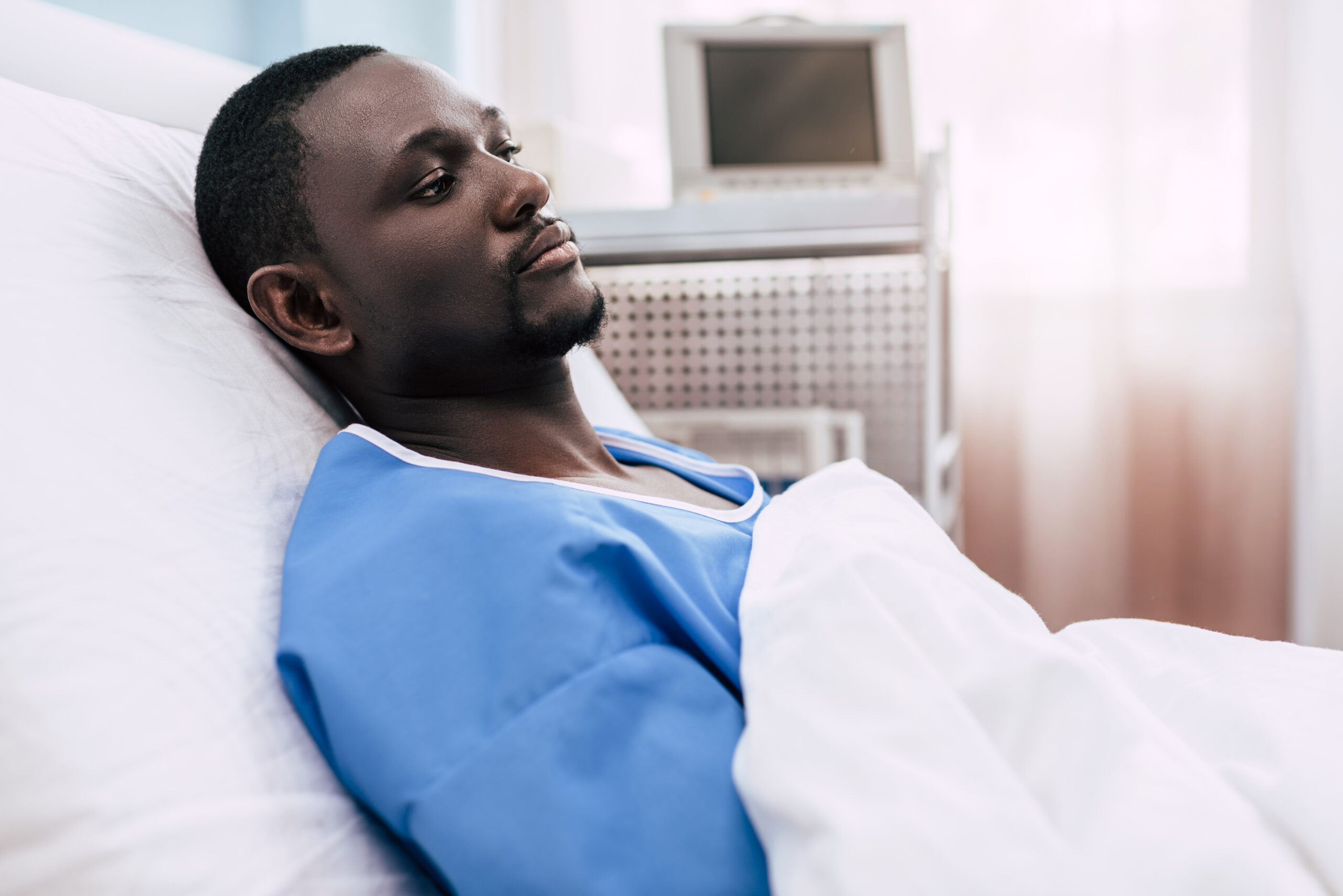 side view of pensive african american man lying in hospital bed