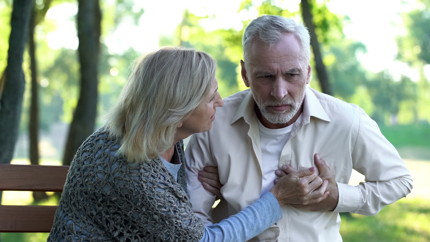 White male clutching his chest with his wife trying to help