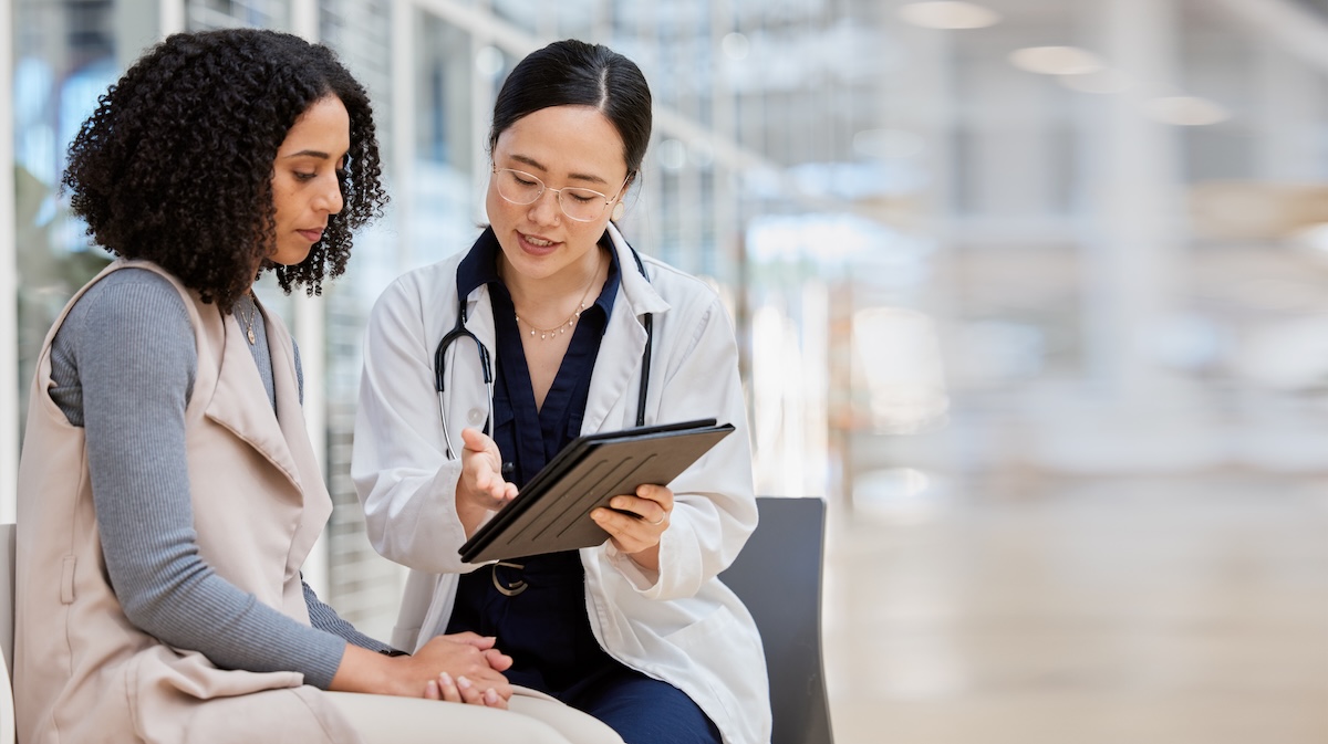 Female doctor and patient reviewing health information together on a tablet during a warm, supportive consultation.