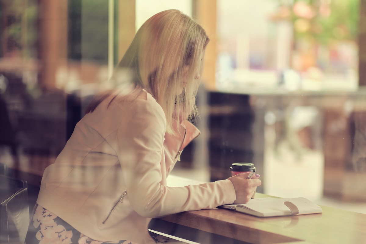 Woman sitting at a table with a journal and coffee cup, reflecting on her health and wellness goals.